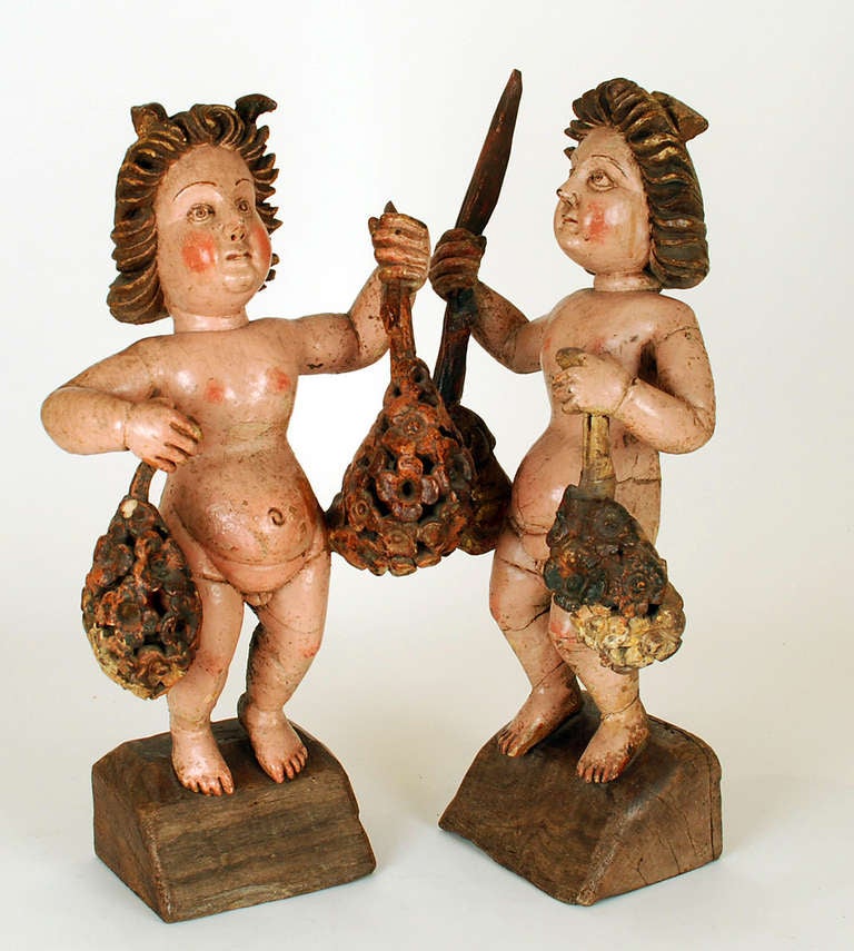 A pair of wonderful early to mid 18th century hand carved and polychrome painted Flemish cherubs, each clutching a pair of gilt-wood and painted flower bouquets. Walnut with original paint, excellent wear and surface patina. Displayed on solid,
