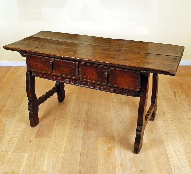 A magnificent 17th Century Spanish Baroque period chestnut desk with a rectangular single board top over a chip carved apron fitted with two short drawers. Raised on scroll shaped legs joined by shaped stretchers; retaining original wrought iron