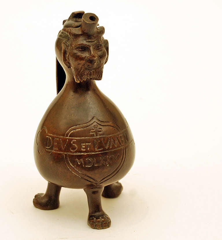 A rare 18th century German made bronze 'Aqua Manille', featuring a troll or gnome with hinged lid and bulbous body terminating into three feet. The body with inscription surmounted by a cross. The Aqua Manille is a particular form of ewer that was