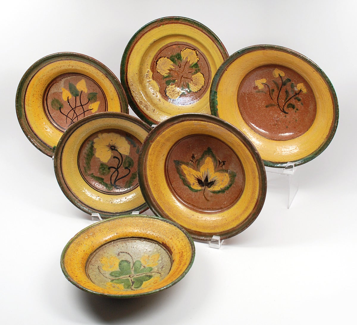 A collection of six turn of the 20th century Guatemalan Majolica plates from the Montiel Family Studio in Antigua, Guatemala. Each plate with whimsical foliate motifs surrounded by colorful yellow and green borders. 

Dimensions: largest measures