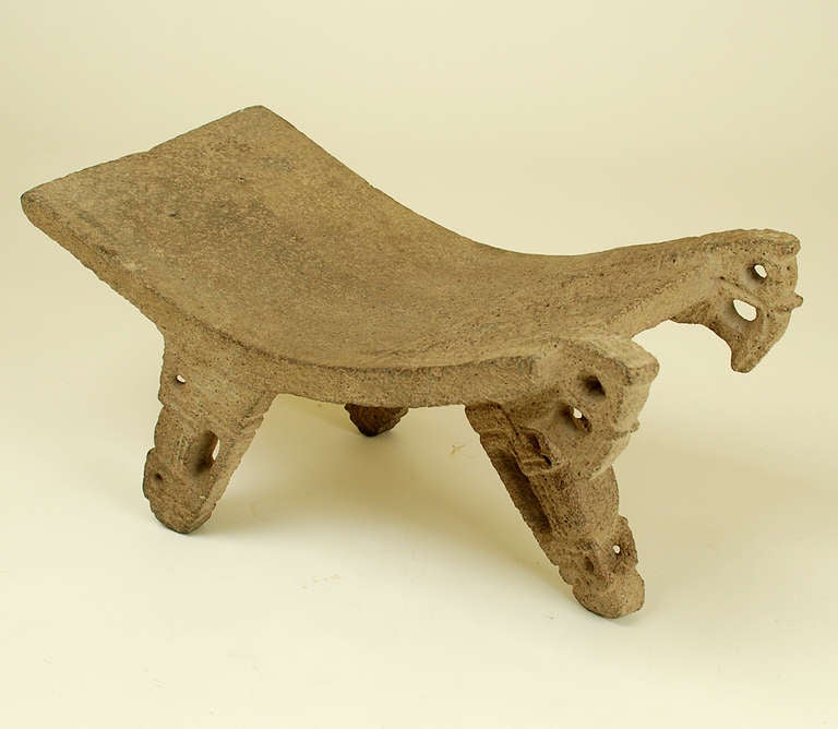 This intricately carved metate from coarse gray stone has a convex, rectangular workbench and is supported by three openwork legs, the whole highlighted by a pair of carved openwork birds at the front. The underside with intricate geometric carving.