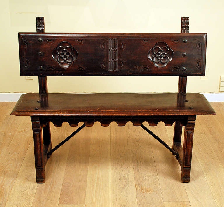 A handsome early 20th century Spanish revival walnut bench with deeply carved rosettes, scalloped edge moulding and large hand forged iron stretcher. Made by the Kittinger Company, Buffalo, NY - circa 1915. Includes custom made cushion.
