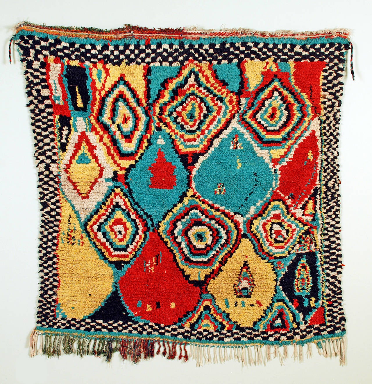 This graphic hand knotted Berber carpet comes from the 'Azilal' province in the High Atlas mountains of Morocco. This rug features a richly colored palette of red, yellow, green and blue circular motifs surrounded by a black and white checkered