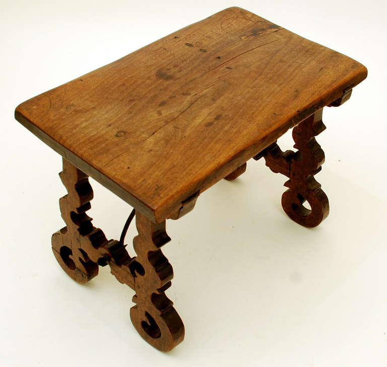 A fine Spanish Baroque period miniature walnut side table, first quarter 18th century, with a thick single board rectangular top raised on scrolled trestle supports and joined by arched iron stretchers. Most likely designed and constructed as a