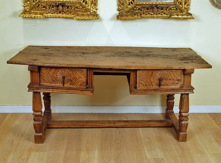 A stunning 17th century Spanish chestnut knee-hole desk with massive single plank chestnut top over two large carved drawers, carved legs and trestle base. Huge square head nails with 1.5 inch nail heads. Carved on all four sides.

Dimensions: 74