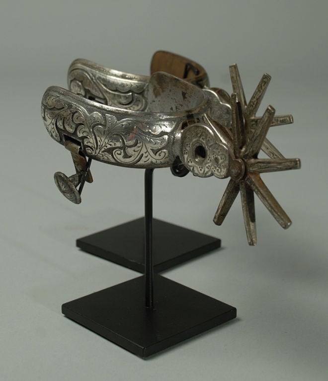 A pair of fancy late 19th century Mexican silver inlaid 'vaquero' spurs with large 3 inch, eight point rowels and 3 inch heel-bands. Beautiful silver work throughout. Displayed on a pair of high quality custom stands.<br />
<br />
Dimensions:
