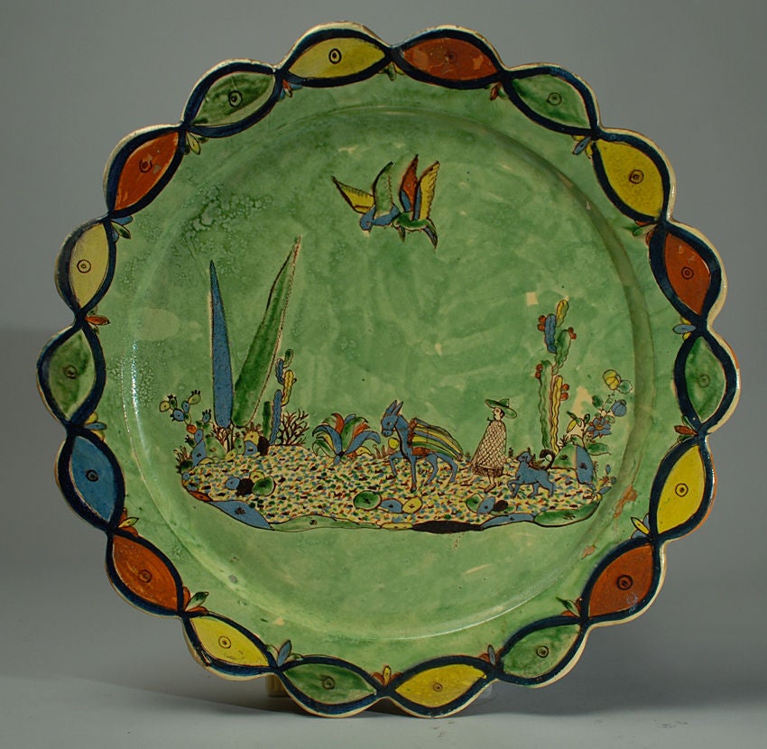 This stunning early 20th century Tlaquepaque 'washy green' charger features a 'campesino,' and his pack mule surrounded by cacti, foliage and colorful parrots. Beautiful scalloped edge with repeating red, green and yellow border. Attributed to