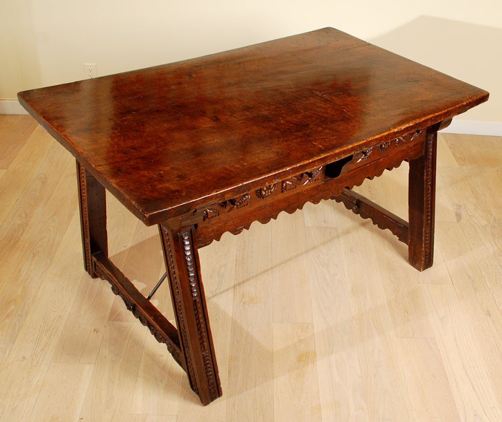 A stunning 17th century Spanish Baroque period walnut center table with large single plank top over a carved apron with two carved drawers - the reverse side of the table with two conforming drawers. Chip carved legs joined by a wrought iron