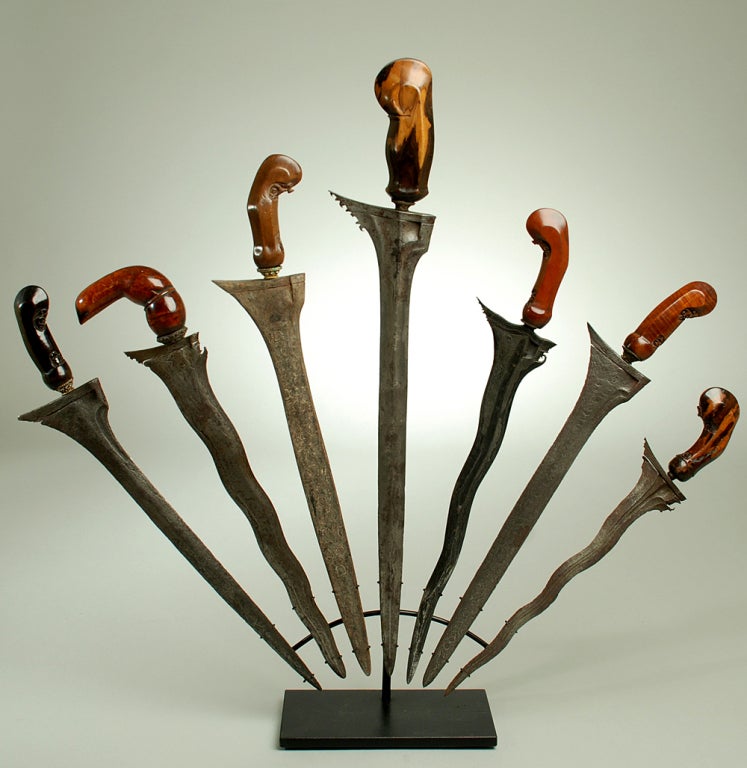 A collection of seven very fine late 19th and early 20th century Indonesian Keris daggers with beautiful hand carved hilts and pamor decorated blades. Displayed in a unique fan pattern on a high quality custom made stand. 

Dimensions: largest