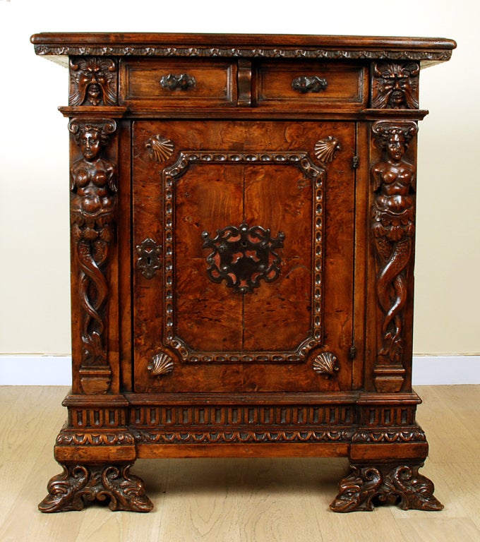 A gorgeous 17th century Italian Baroque Walnut Credenza with a rectangular top over two drawers and a paneled door. Beautiful matched walnut veneer door with original hand forged iron escutcheon flanked by a pair of magnificent hand carved mermaids