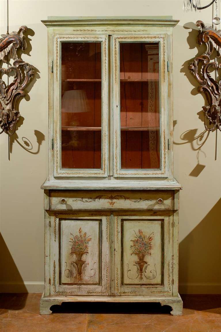 Italian paint decorated secretaire, the corniced top surmounting two glass doors opening to reveal three shelves above a single drawer, all above a double door cabinet opening to reveal two shelves and raised on bracket feet, with all over floral