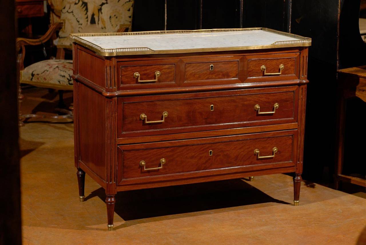 19th century Louis XVI style commode, the inset white variegated marble top with brass gallery rim surmounting three drawers and raised on turned fluted legs.