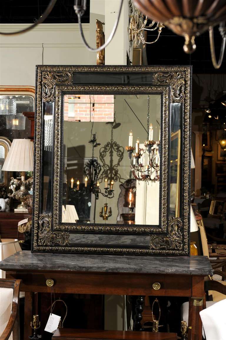 Fine rectangular mirror framed in embossed brass and ebonized wood.  Beautiful worked brass floral designs frame both the inner and outer mirrors and the corners are decorated with acanthus leaf motifs.  The interior mirror has a beveled edge.