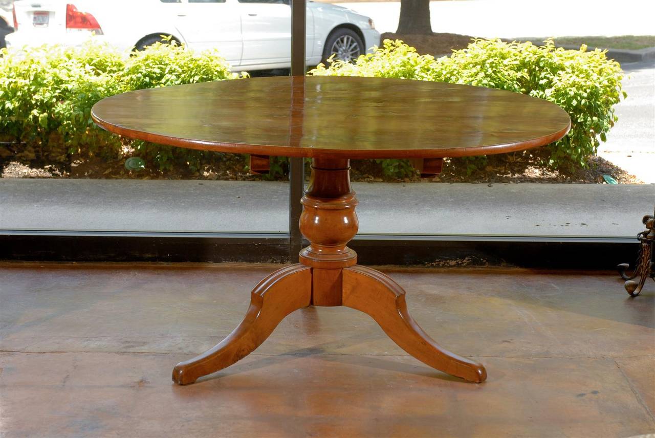 An Italian mid 19th century fruitwood round dining table with tilt top, turned pedestal base and tripod legs. This Italian 1850s dining table features a circular top over a nicely turned pedestal, resting on three curved and splayed legs. The table