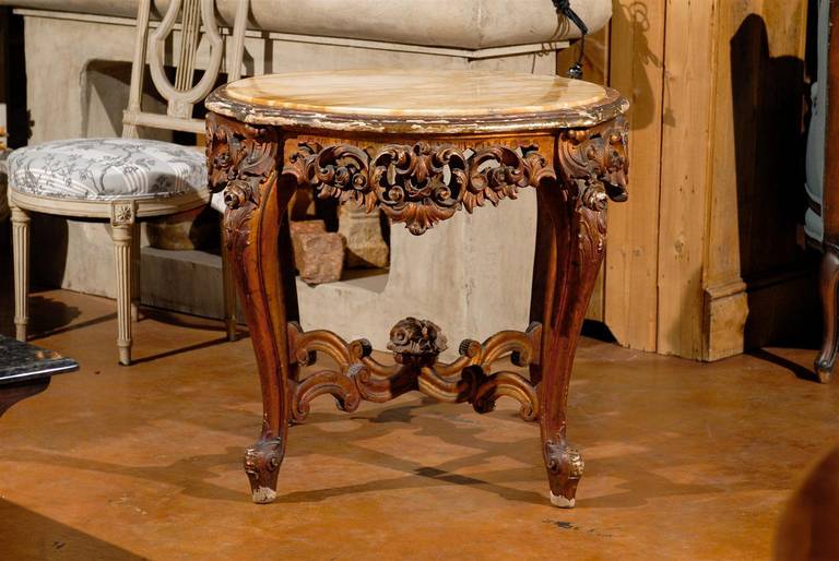 An Italian Rococo style round side table with Siena marble over a richly carved base from the 19th century. This exquisite Italian side table features a “giallo Siena” marble top (yellow veined marble) over a hand-carved, painted base. The apron is