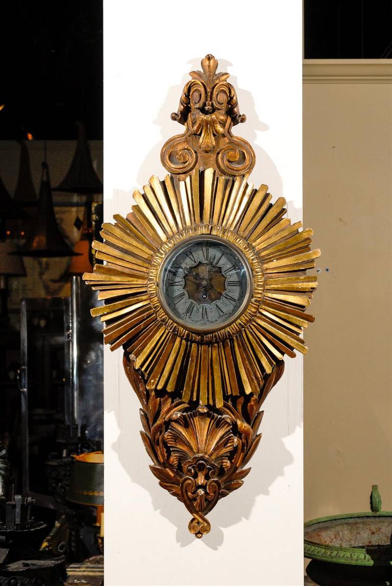 19th century French carved giltwood starburst clock, the scrolling crest surmounting a circular face with strips of giltwood emerging to allude to the sun, terminating in floriform carving. 