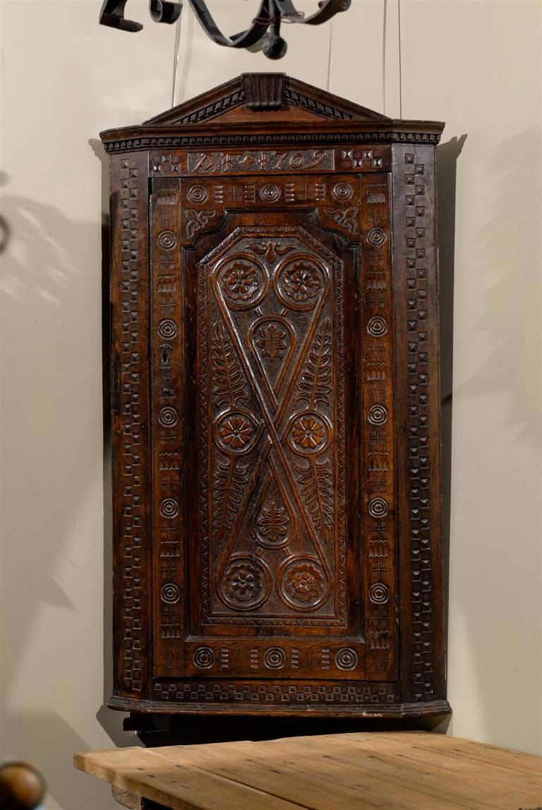 Early 18th century English carved corner cupboard, the pediment crest surmounting one long door with elaborate carving opening to reveal four shelves, with three small drawers between the lowest and second lowest drawer lined with green felt and