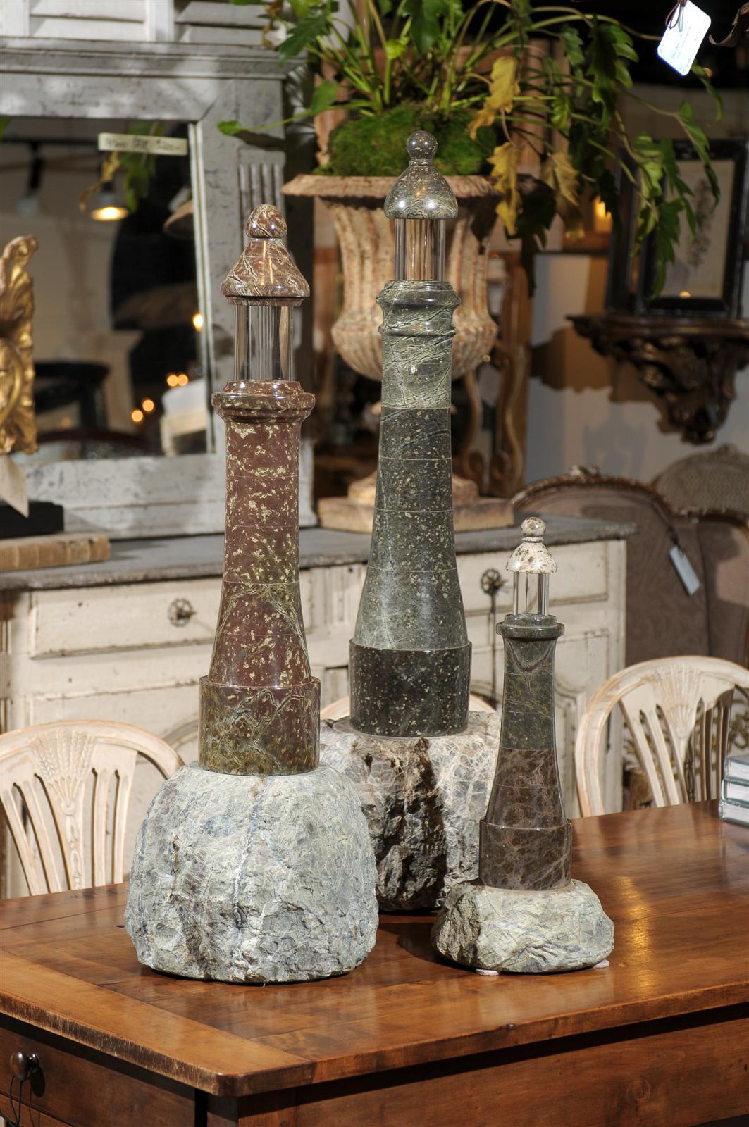 A set of three English grey and reddish-brown veined marble and stone decorative lighthouse figurines from the late 19th century. These English decorative objects feature three similar looking stepped marble lighthouses raised on stone bases of