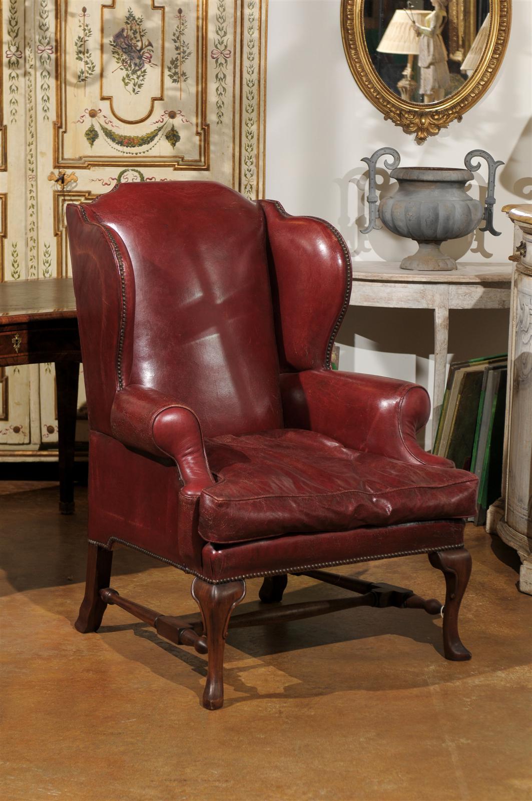 Late 19th century English wingback chair, the red leather upholstered shaped back surmounting a conforming seat, raised on cabriole legs and joined by an H-form stretcher, with nail trim throughout.