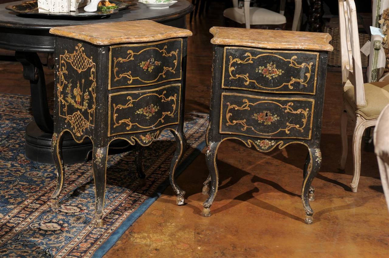 A pair of Italian rococo style Florentine black painted Chinoiserie commodes of petite size from the late 19th century. Each of these Italian commodini features a warm yellow marbleized top tracing  the shape of the serpentine two-drawers front. The