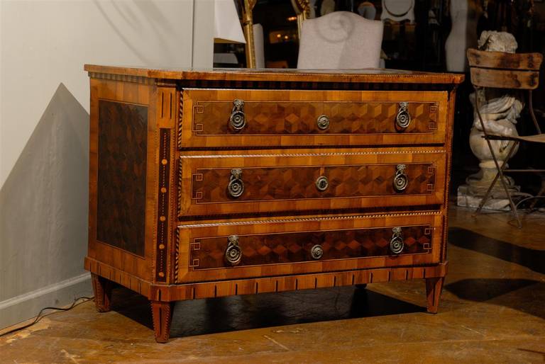 Early 19th century French commode, the inlaid rectangular top with canted corners and inlaid sides of geometric shapes surmounting three long drawers raised on elongated spade feet, with similar inlay throughout.