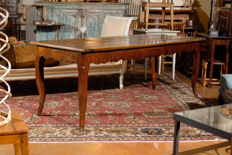 A French fruitwood farm table with cabriole legs and scalloped apron from the 19th century. This French farm dining table features a four-plank rectangular top framed with additional boards, over a nicely scalloped apron on all sides. The table is