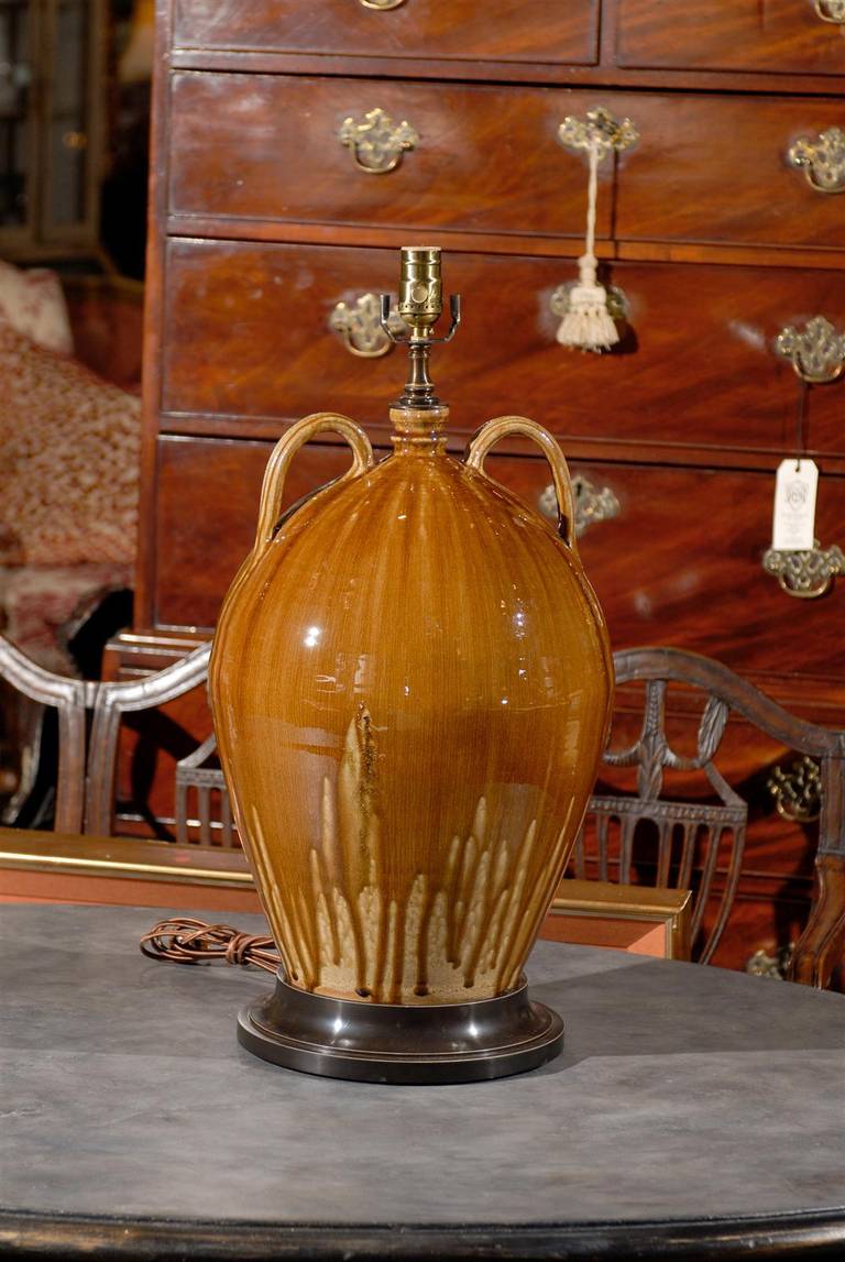 Handmade North Carolina ceramic double-handed jug as lamp, with drip glaze and raised on a circular stepped base. 