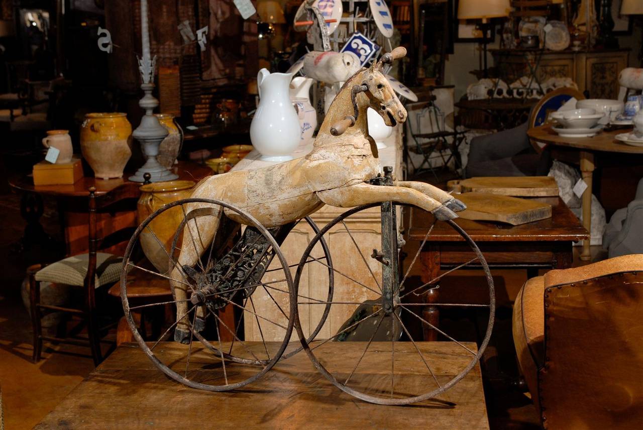 A French carved horse on wheels from the late 19th century. This French wooden sculpture circa 1880 features a carved and painted wooden horse that seems to be riding a tricycle. The handlebars are placed on each side of the head and the pedals are