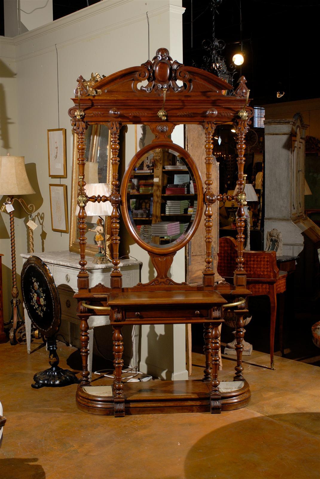 French walnut hall tree with central mirror, the elaborate pediment crest surmounting a central oval mirror flanked by double turned columns on each side, above a step front central single drawer, raised on turned legs and a conforming plinth with