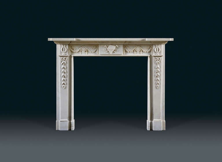 The breakfront moulded tiered shelf breaks over the jambs; the frieze is centered with an oblong tablet, and is sculpted with crossed, ribbon tied horns and overlaid with Pan's graduated pipes, the syrinx. Flanked by panels with circular flower