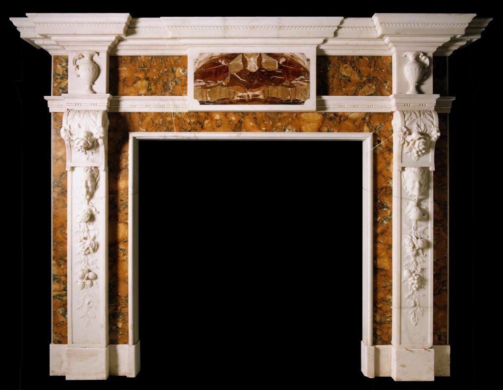 A magnificent mid-18th century chimneypiece in statuary marble with heavily carved foliate pilasters headed by masks. Carved trusses support corner blocks carved with ewers. Richly figured convent Sienna marble flanks the pilasters and the central