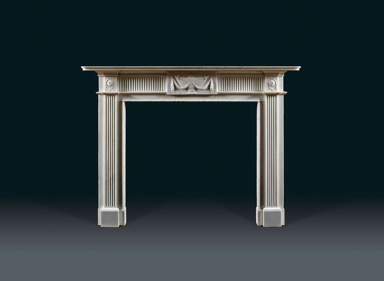 A neoclassical, late 18th century, statuary marble chimneypiece. The moulded shelf has rounded corners above the frieze which is centered with a tablet carved with a tazza shaped lidded urn with leaf decoration on a sickle decorated with running