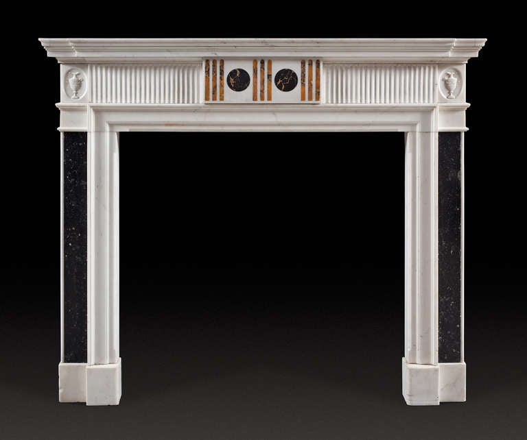A late 18th century Kilkenny and statuary marble chimneypiece, possibly Irish. The moulded tiered shelf, fluted frieze centered with a tablet inlaid with sienna flutes and portoro roundels. The pilaster jambs inlaid with panels of polished Kilkenny