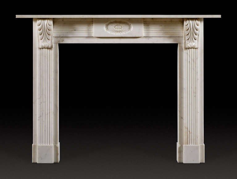 A statuary marble chimney piece of typical early 19th century, English Regency design. The rectangular shelf with reeded edge, above the frieze which is centered with an oblong tablet carved with an oval medallion of a flower head, flanked by convex