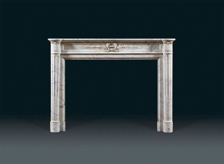 A Louis XVI Carrara marble chimneypiece the rectangular top with rounded corners, French, circa 1870. The frieze with inset moulded panel carved with two lilies tied with bowed ribbons to sprays of laurel, symbolic of peace and victory. The jambs in