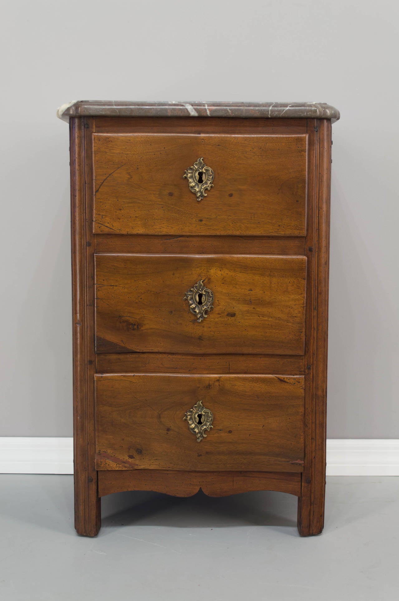 An 18th Century Louis XV style petite commode or chest of drawers, made of walnut with waxed finish. Three dovetailed drawers with curved front and raised panels on the sides. Original marble top (repaired). Nice size for use as a nightstand. As