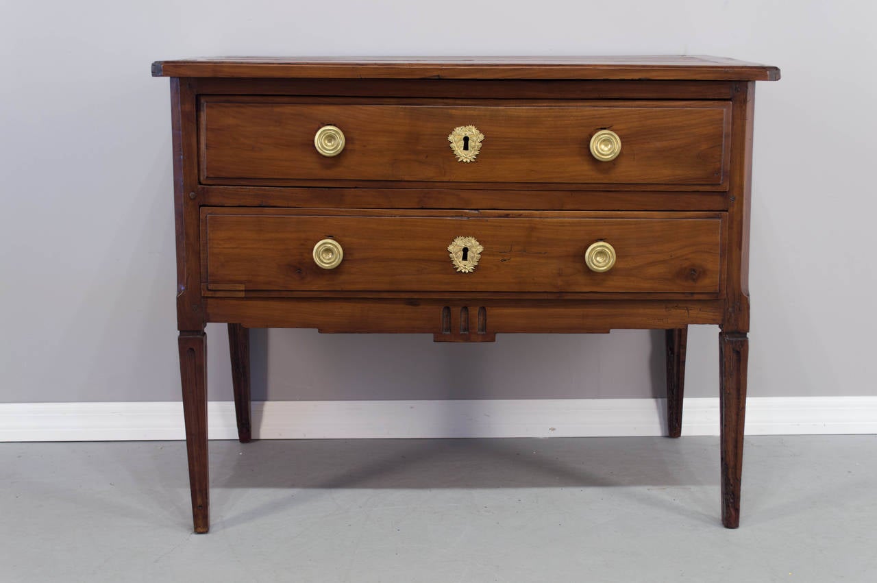 A solid cherry 18th c. Louis XVI commode with two large dovetailed drawers, two raised panels on the sides, fluted legs probably from the Nantes province (Loire Valley). Pegged construction and wax finish. Polished hardware is not original but of