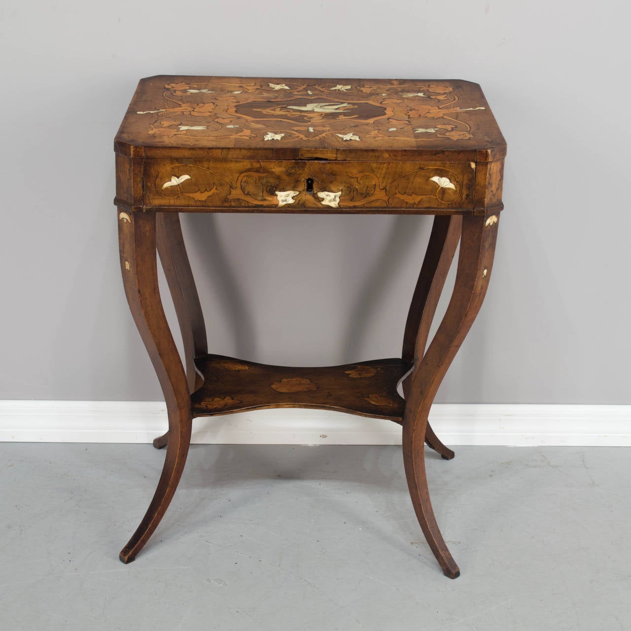 A 19th century Italian side table made of walnut and cherry with bone inlay. Beautiful marquetry decoration with entwined vines and flowers surrounding a  white dove. One dovetailed drawer with divided compartments. Curved legs and lower shelf.