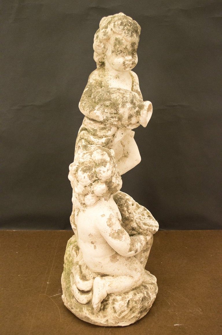 A garden sculpture representing two cherubs, on holding an amphora where the water pours out and the seating cherub holds a shell. Good surface with appropriate moss. The statue weighs 115 lbs.
