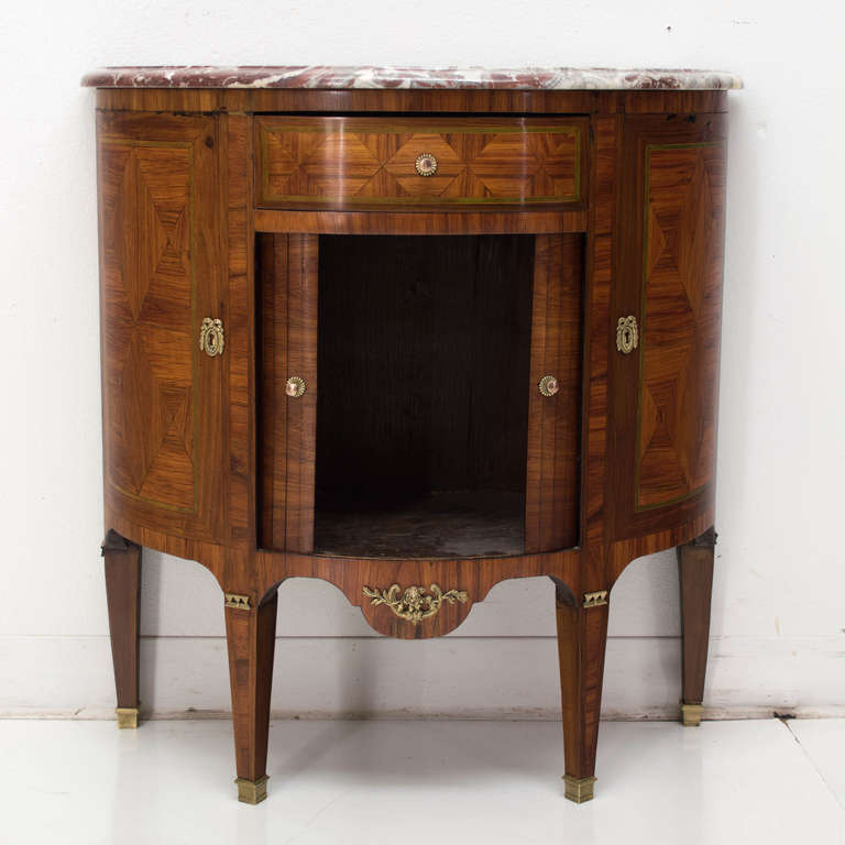 In a half moon form, this fine marquetry cabinet has two tambour doors below a  dovetailed drawer and topped with a rouge beveled marble top, decorated with bronze hardware.
Mostly mahogany, walnut and cherry veneer.