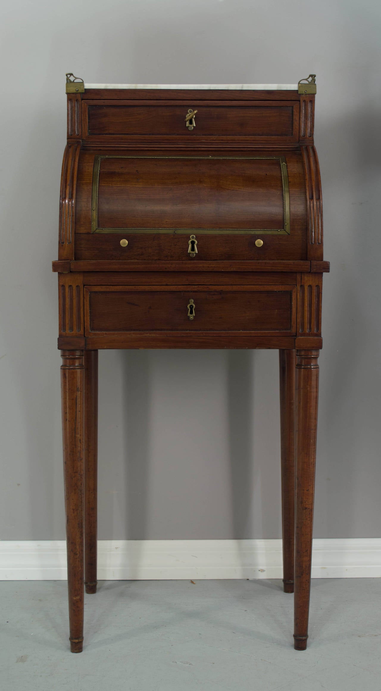 A nice small 19th century Louis XVI style desk, made of mahogany with dovetail construction. Marble top surrounded by a brass gallery and bronze hardware. Two locking drawers in working order with one key. Desk rolls open and pulls out to reveal a