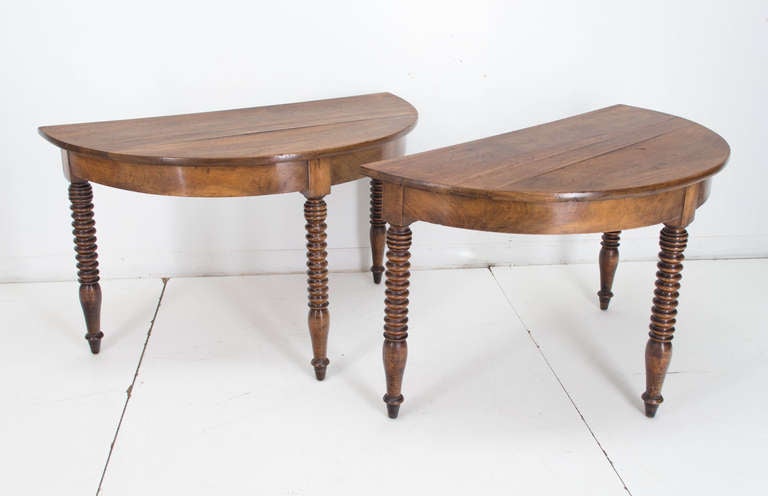 A pair of solid walnut consoles each having three turned legs. Originally this type of table was used as a dining table. Each leg had ended with a caster which is missing. The size for one console is 45