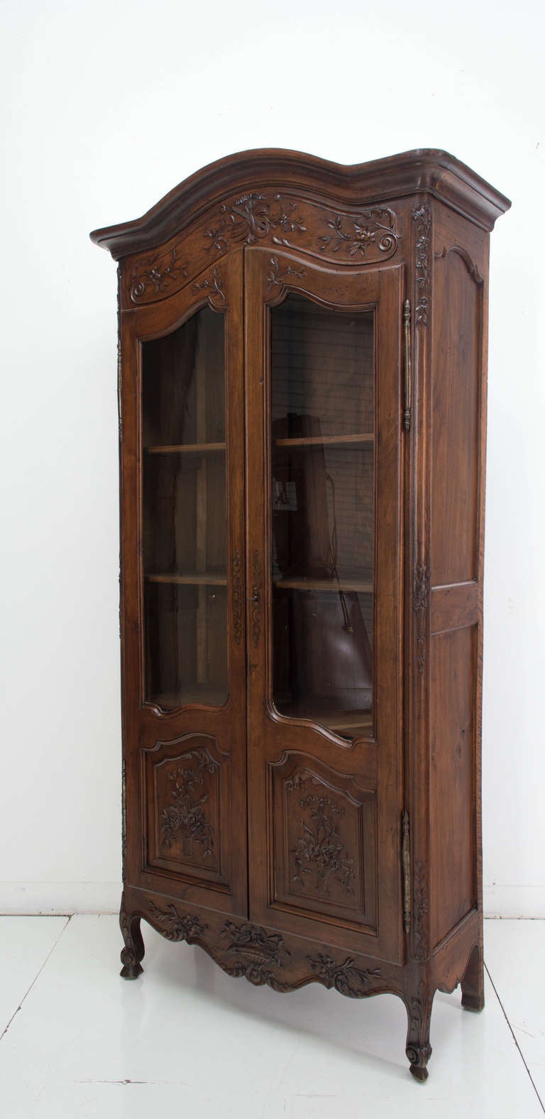 A vitrine from Provence  made of walnut with two glass panel doors, carved panels above a shaped apron ended with two front scrolls toes legs, Chapeau de Gendarme Crown, (curved crown) removable, three shelves inside with an inside depth of 13