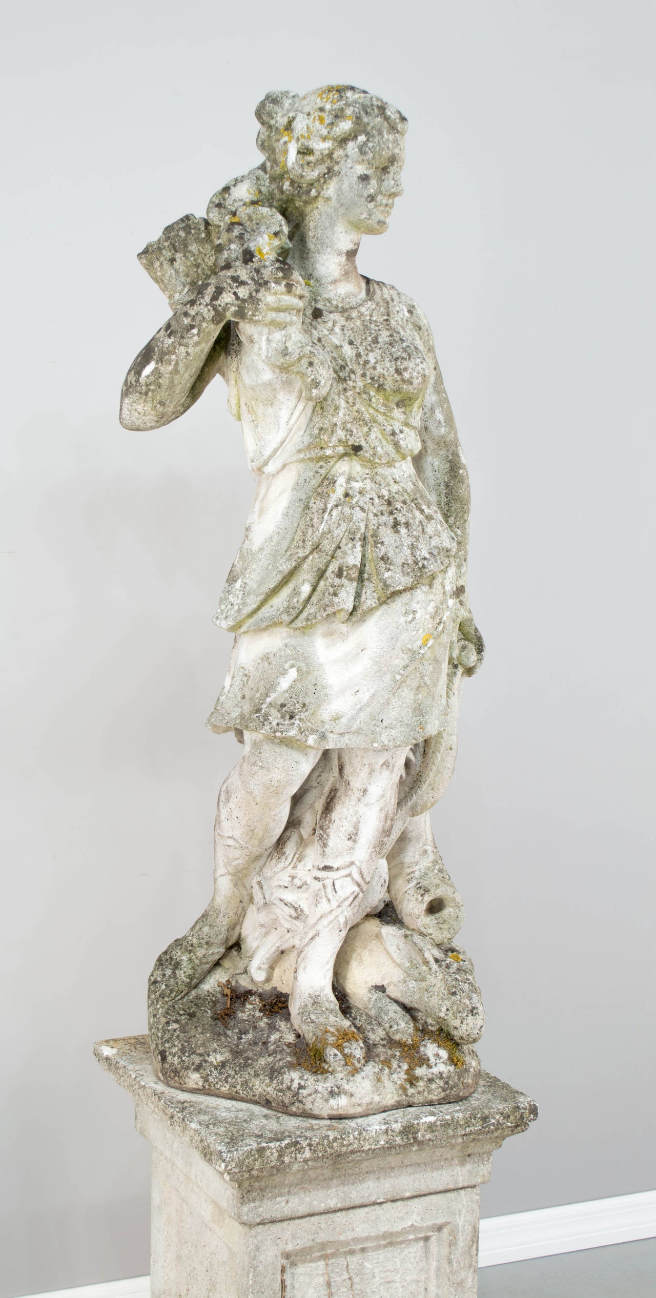 French cast stone garden statue of the Greek goddess, Diana the Hunter, depicted holding her bow at her side, a quiver over her shoulder and a rabbit at her feet. Very detailed and with nice old mossy patina. This large statue rests on a separate