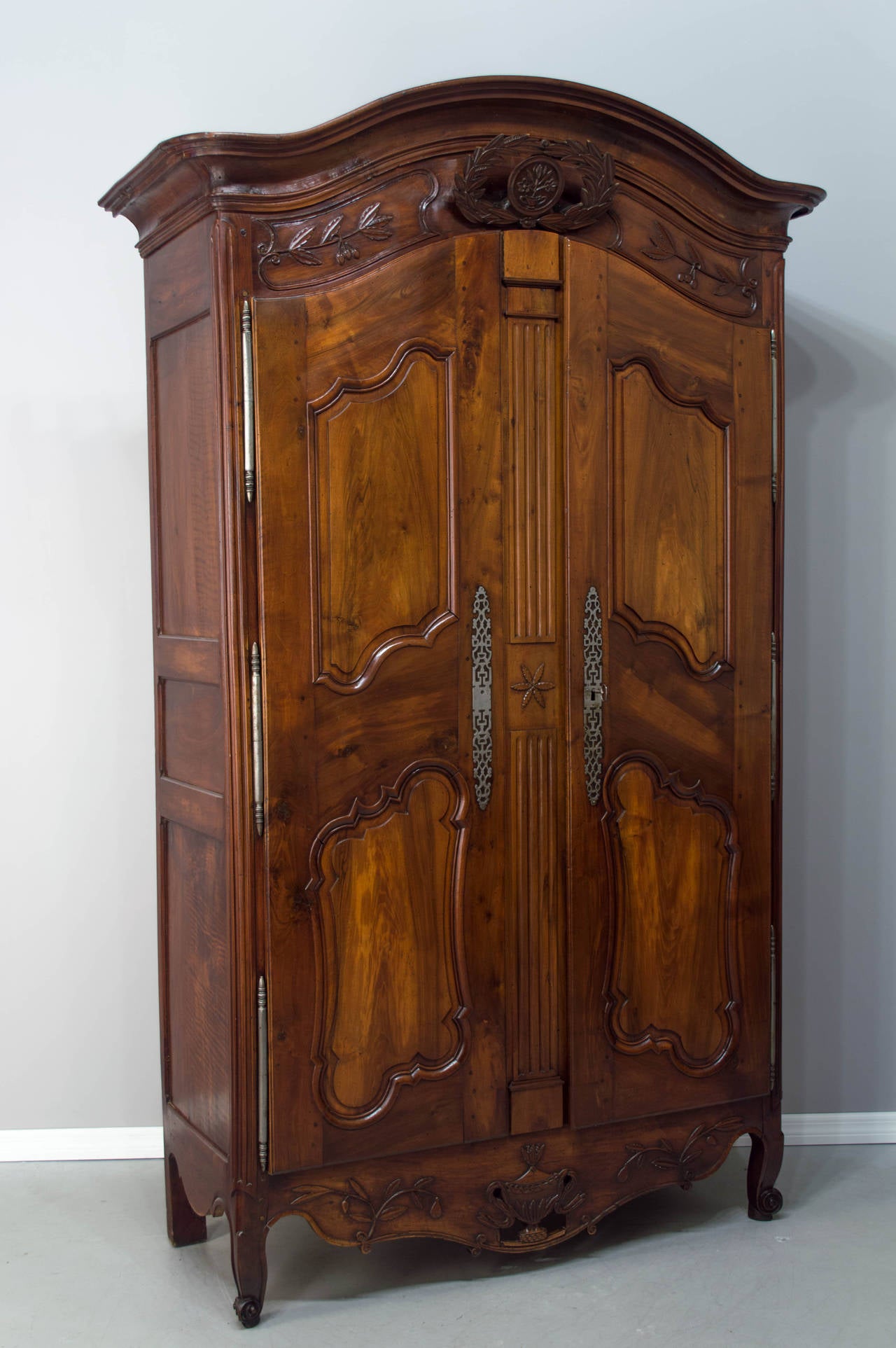 An 18th century bridal armoire from Provence, made of solid walnut with a chapeau de gendarme crown above a hand-carved olive wreath. Two doors having two raised panels each, opening to three shelves, one having a set of two drawers and below, a