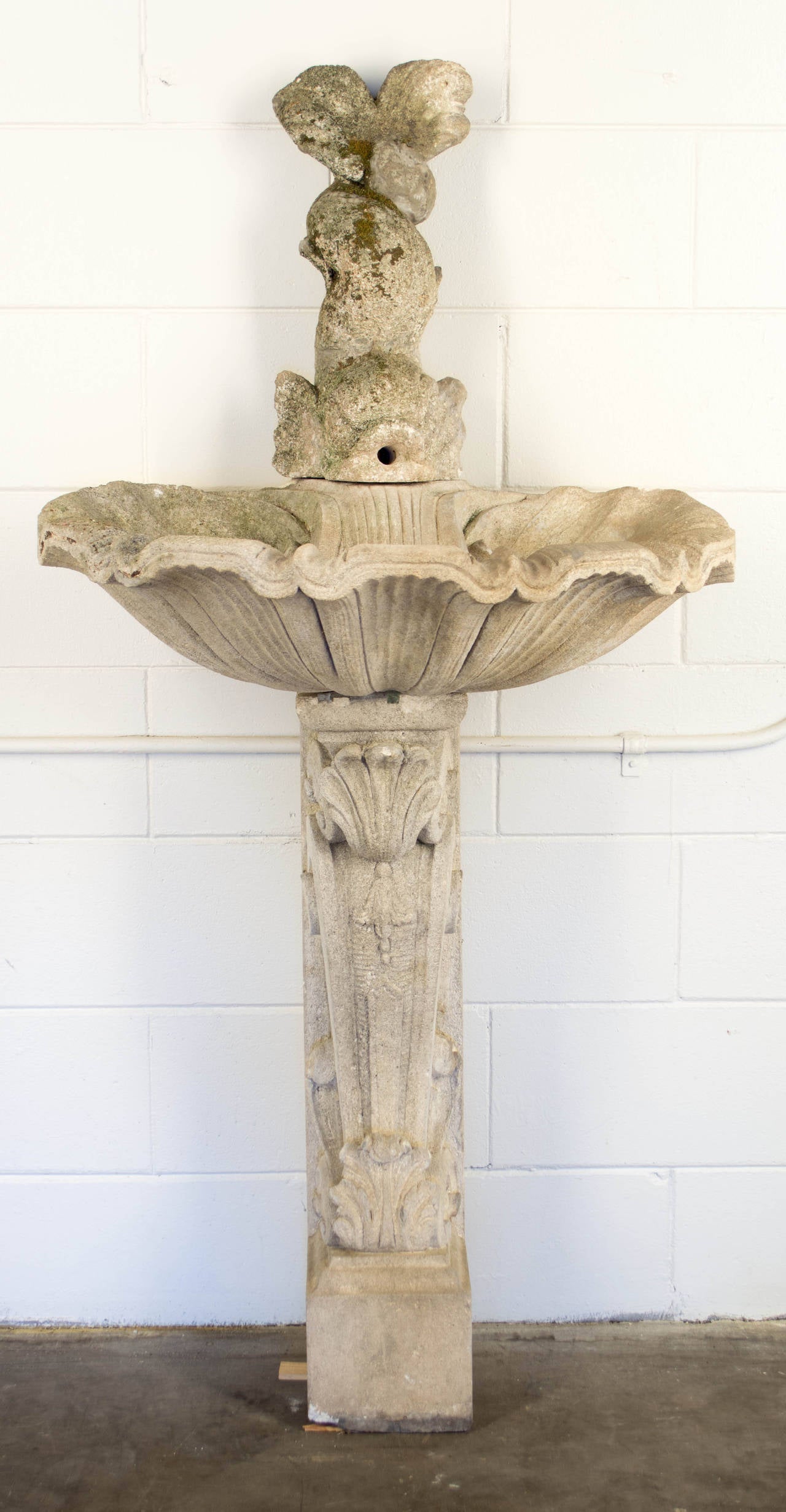 A country French stone fountain from Provence. In three parts with carved scrolls and acanthus leaves forming the pedestal base, a shell shaped basin and dolphin spout. Nice old patina and moss. As always, more photos available upon request. We have
