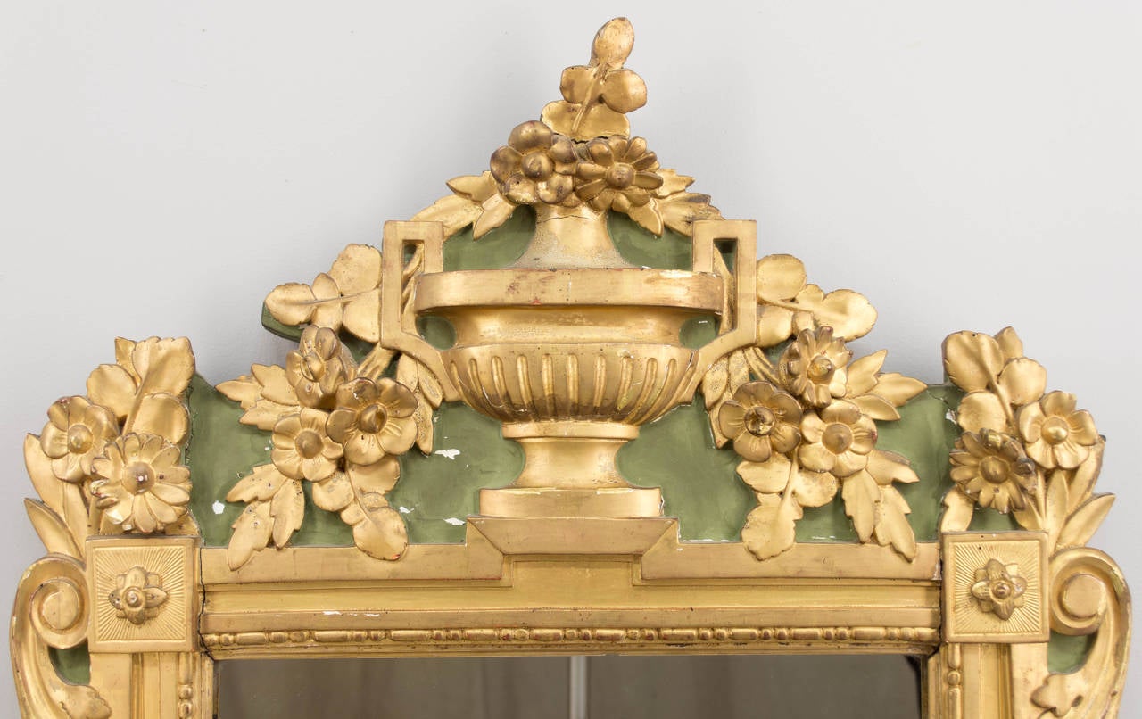 18th century French Regency style gilt and painted mirror. Very sculptural, with a four inch depth of the classical style urn at the top. Beautifully carved flowers with scrolling athanthus leaves draping along the sides and rosettes in the corners.
