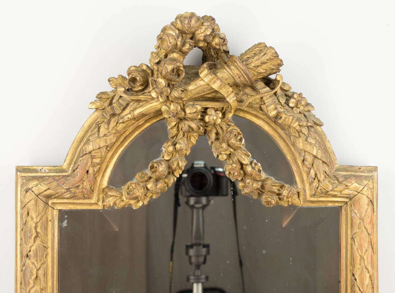A 19th century French Louis XVI style mirror with hand carved and gilded wood frame. A full-length dressing mirror with tall narrow proportions. Original looking glass with a one inch bevel. Beautifully detailed wood carvings of flower garlands and