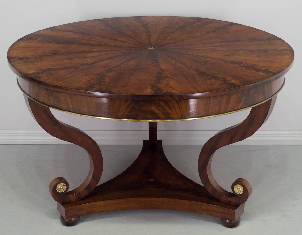 Exceptional early 19th century French gueridon or center table made of flamed mahogany veneer with bookmatched top. Elegant, graceful curved legs decorated with brass medallions. Curved triangular base is also bookmatched, with bun feet and small
