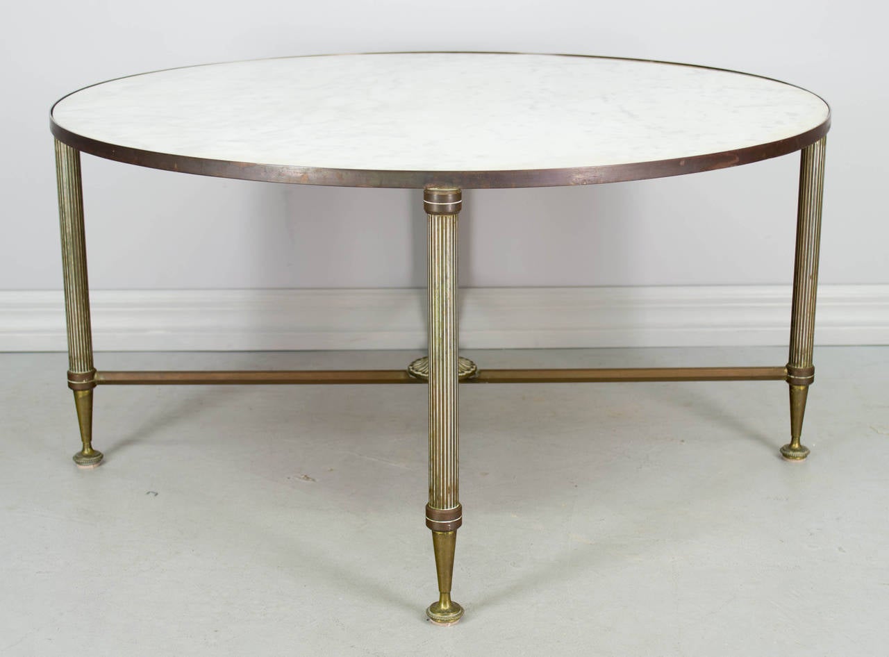 French 1940s circular coffee or cocktail table made of brass with nice warm brown/greenish patina. X-stretcher base with center rosette. White marble top. More photos available upon request. We have a large selection of French antiques. Please visit